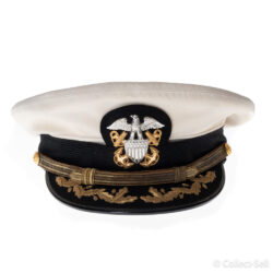 A U.S. Navy officer’s white combination cap with a black visor embroidered with gold oak leaves and acorns. The cap features a silver eagle insignia with crossed anchors and a gold chin strap held by buttons engraved with the Navy emblem.